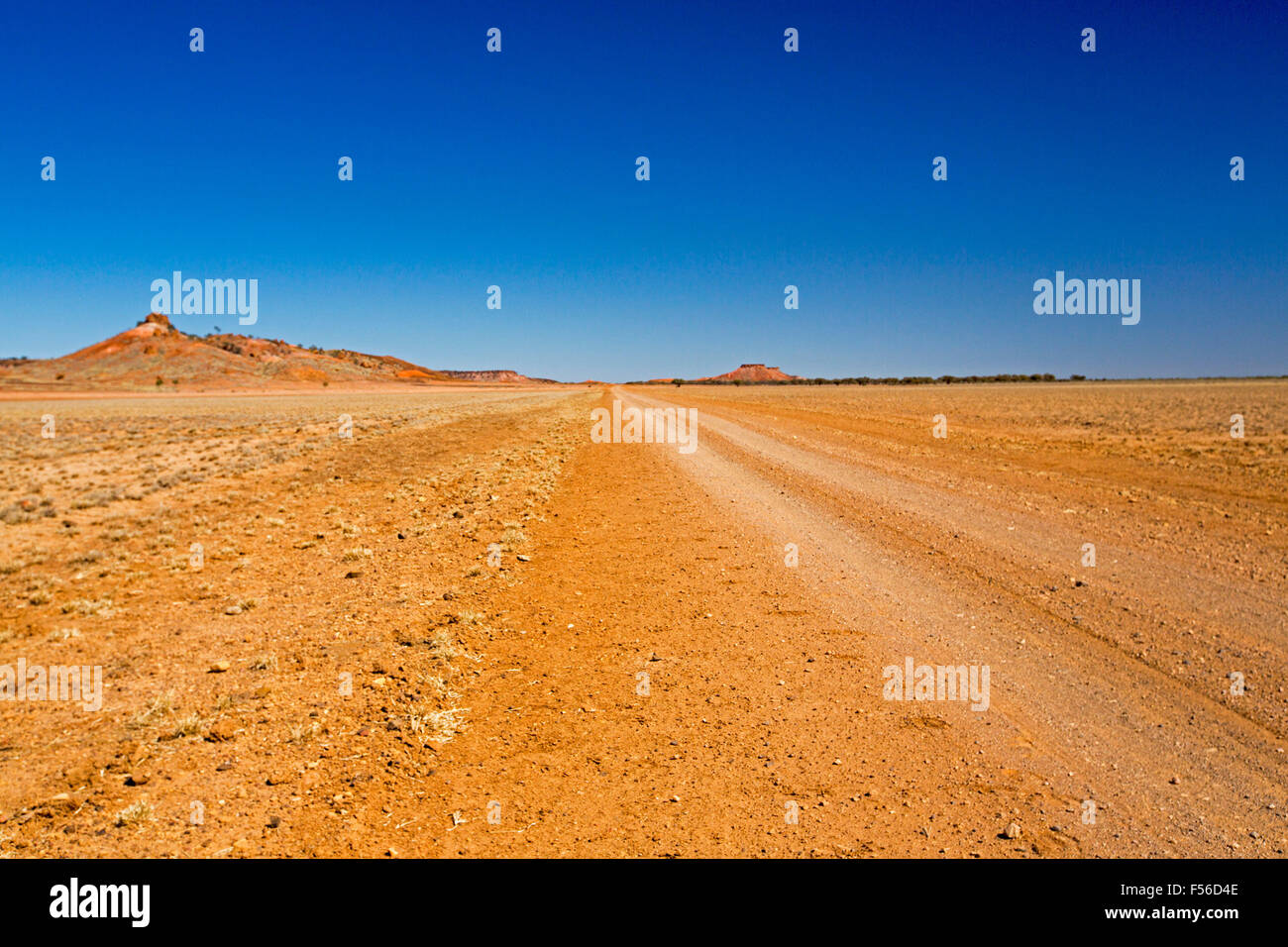 Largo camino de tierra outback todo desarbolado rojo llanuras con colinas bajas en el distante horizonte bajo un cielo azul, en el oeste de Queensland Australia Foto de stock