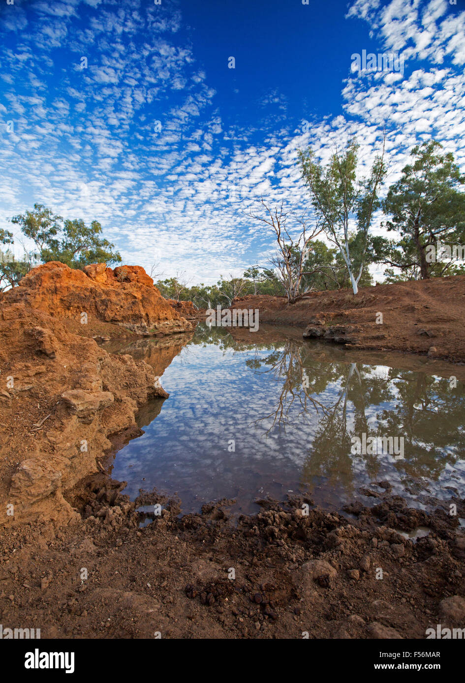 Impresionante paisaje outback, cielo azul con nubes pecoso se refleja en la superficie del espejo de agua rodeado por escarpadas rocas rojas Foto de stock