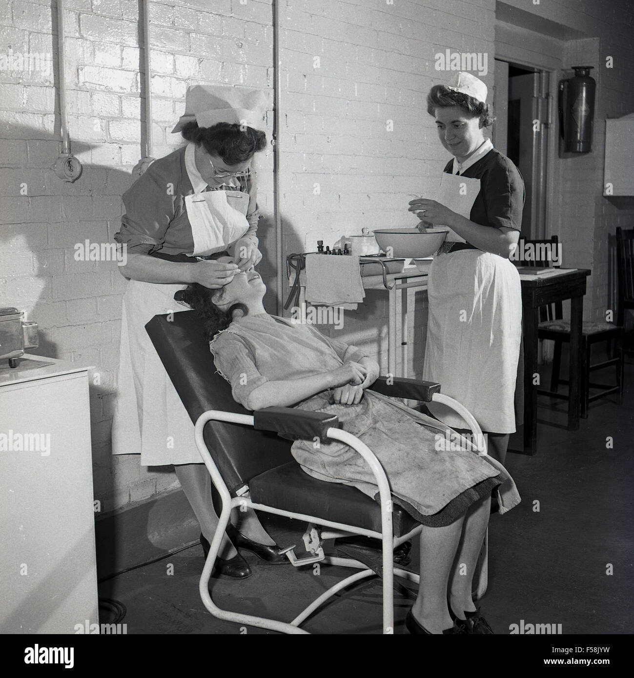 1950, foto histórica, un joven trabajador de la fábrica en su monos sentado  en una silla con la atención médica, la boca y los dientes que están siendo  examinadas por la labor