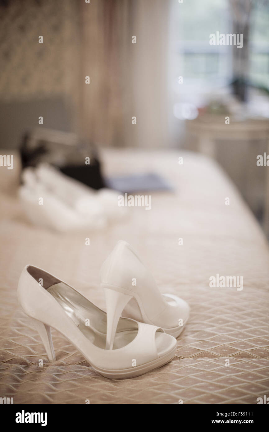 Color digital artística foto vertical rectangular de color blanco de la  novia zapatos de tacón en la cama en el dormitorio suite de hotel de lujo.  Profundidad de enfoque con un fondo