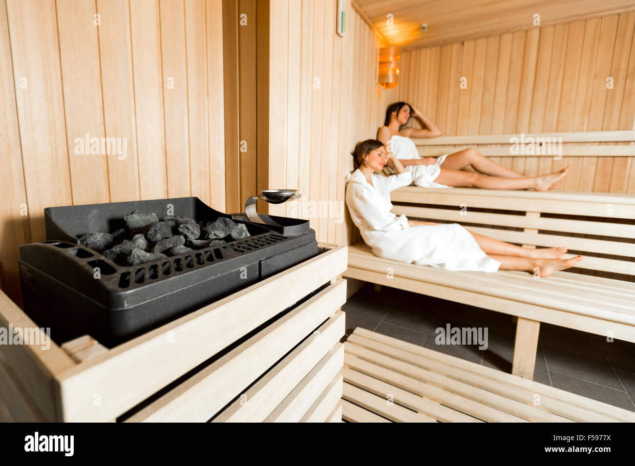 Sauna calentador en una acogedora sauna y niñas relajante en el fondo Foto de stock