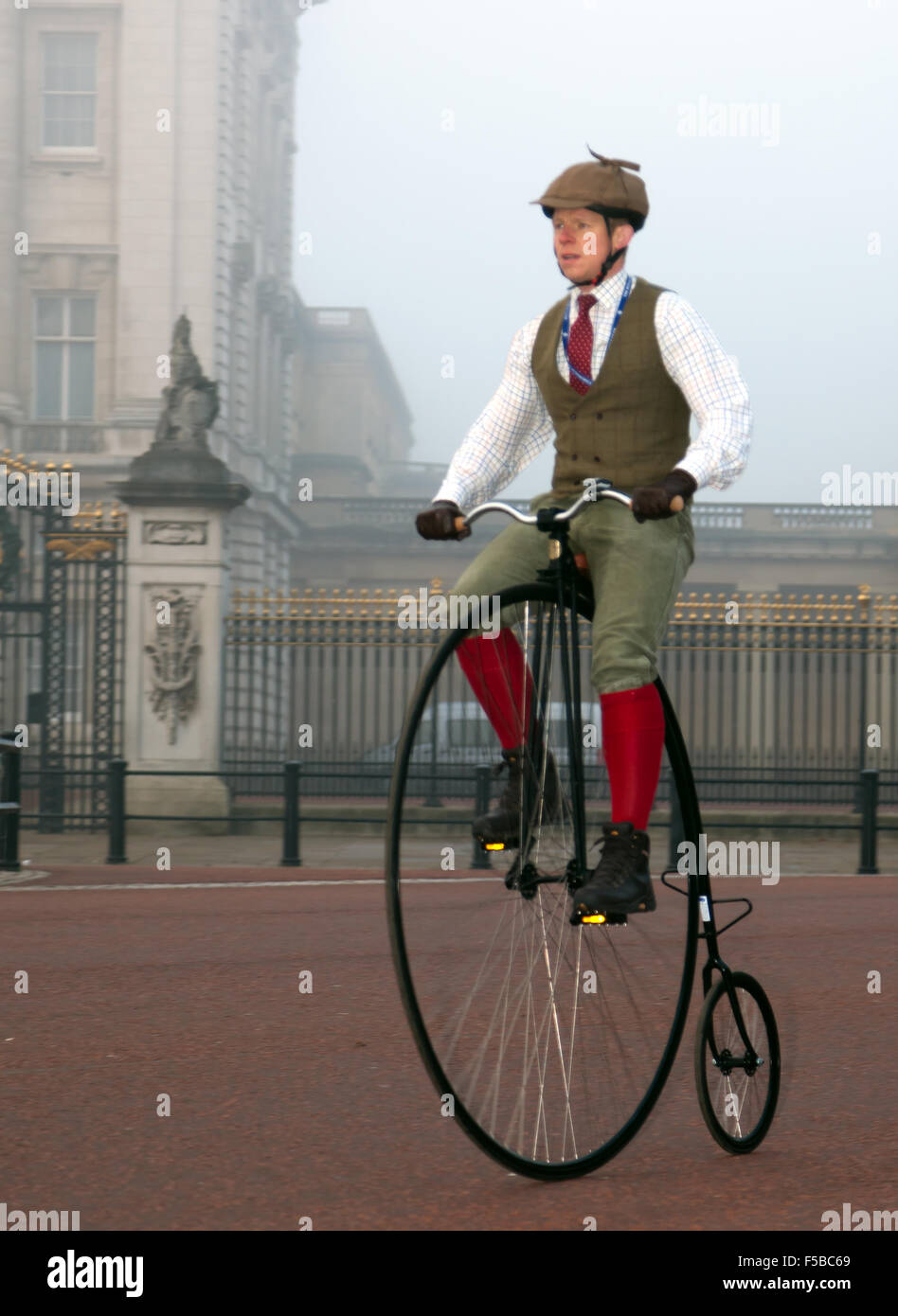 Un hombre, con trajes de época de ciclos pasados Buckingham Palace, sobre un antiguo Penny-farthing, durante el London to Brighton veteran Car Run. Foto de stock