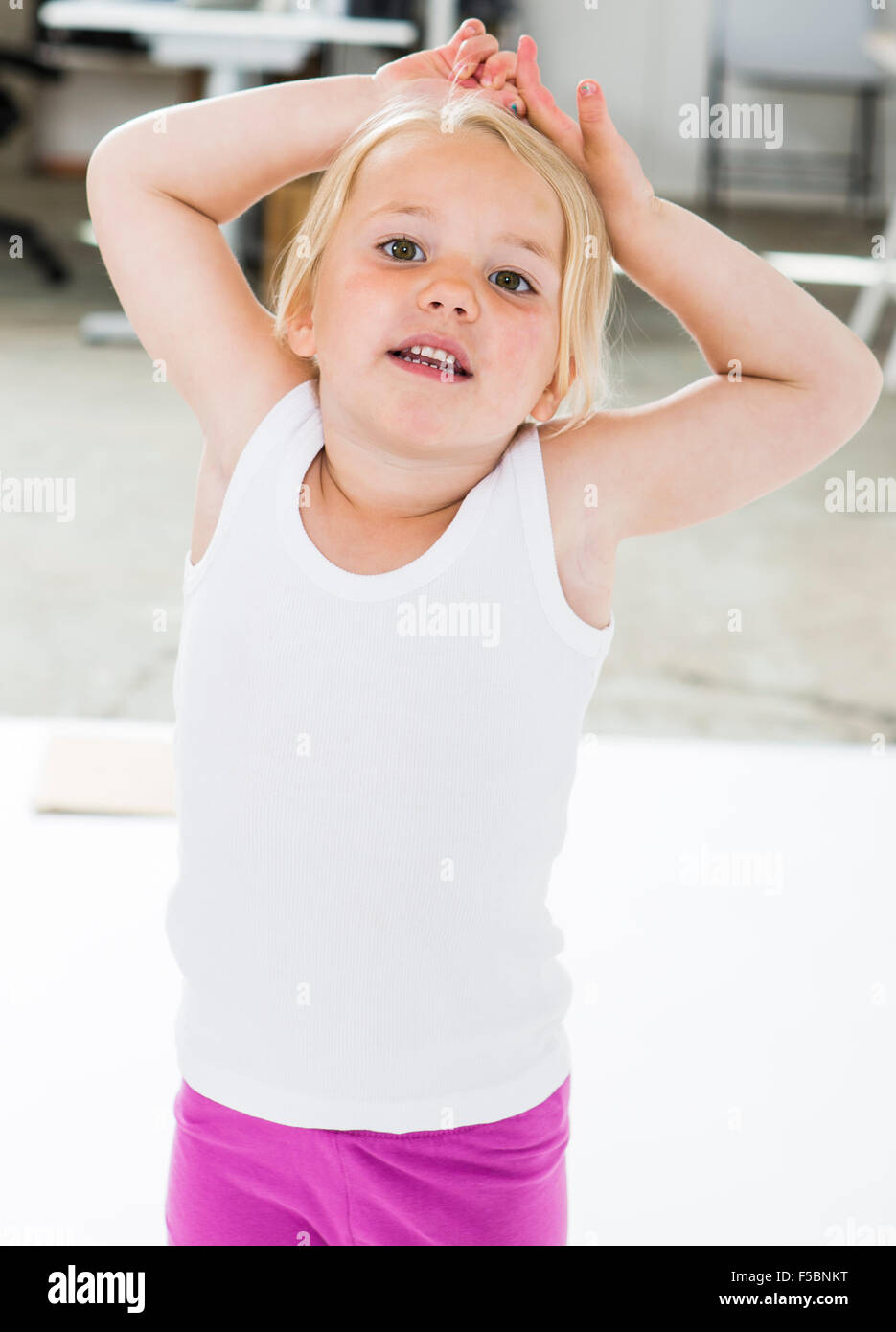 Cuatro años de edad, niña de pie con las manos y los brazos por encima de su cabeza, mirando a la cámara. Foto de stock