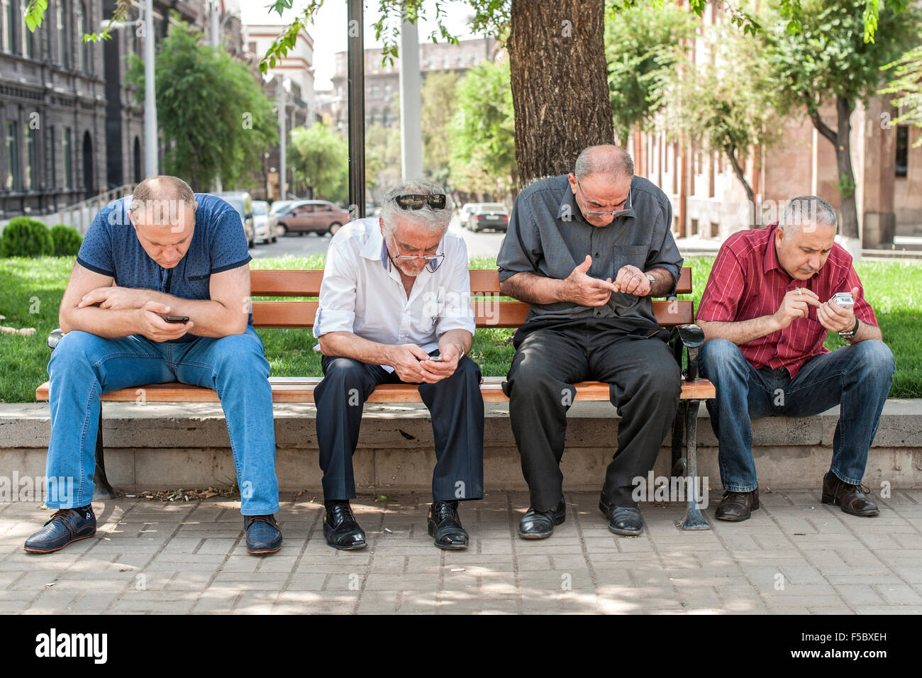 Cuatro hombres con sus teléfonos inteligentes en un parque en Ereván, la capital de Armenia. Foto de stock