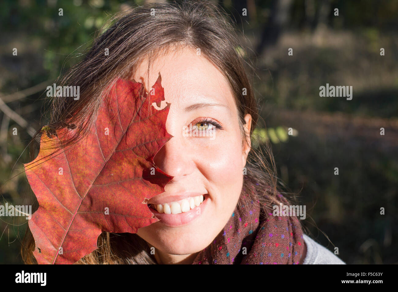 Retrato de belleza de otoño al aire libre. Chica con hermosos ojos verdes holding red hoja de otoño sobre su cara en el parque Foto de stock