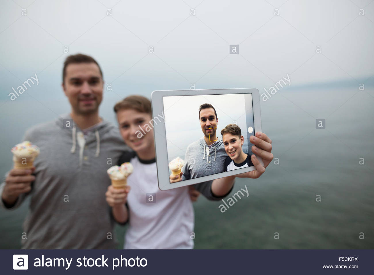 Padre hijo comer helado teniendo selfie lakeside Foto de stock