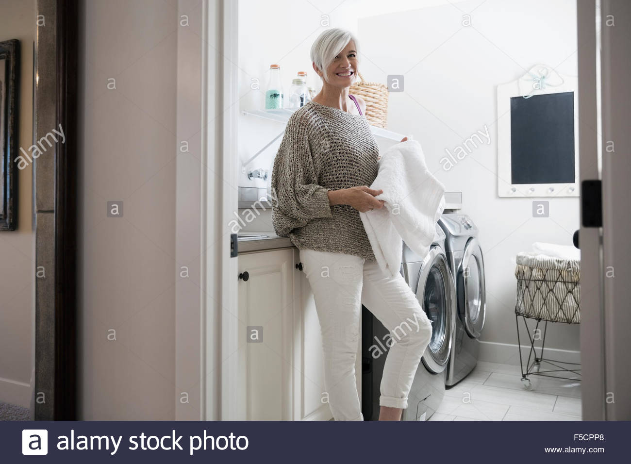 Retrato mujer sonriente toallas de plegado en cuarto de lavandería Foto de stock