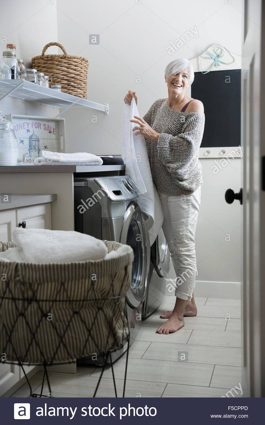 Mujer sonriente toallas de plegado en cuarto de lavandería Foto de stock