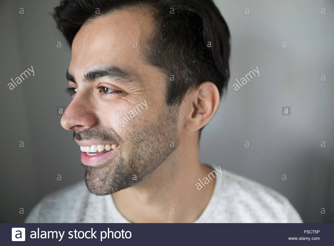 Hombre sonriendo con cabello negro en busca de rastrojos lejos Foto de stock
