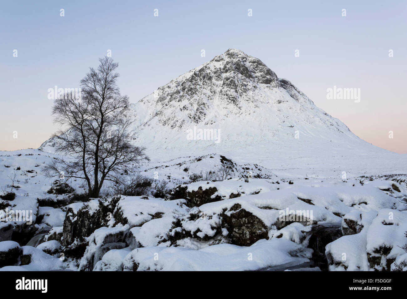 Buachaille Etive Mor en Glencoe, Escocia, cubierto de nieve con una cascada congelada en primer plano. Foto de stock