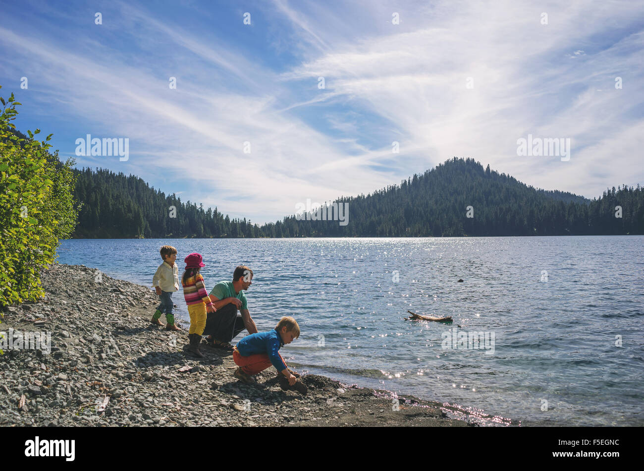 Hombre con tres niños jugando por un lago Foto de stock