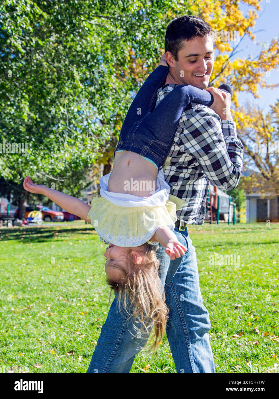 Padre festivamente llevar hija joven boca abajo en el parque Foto de stock