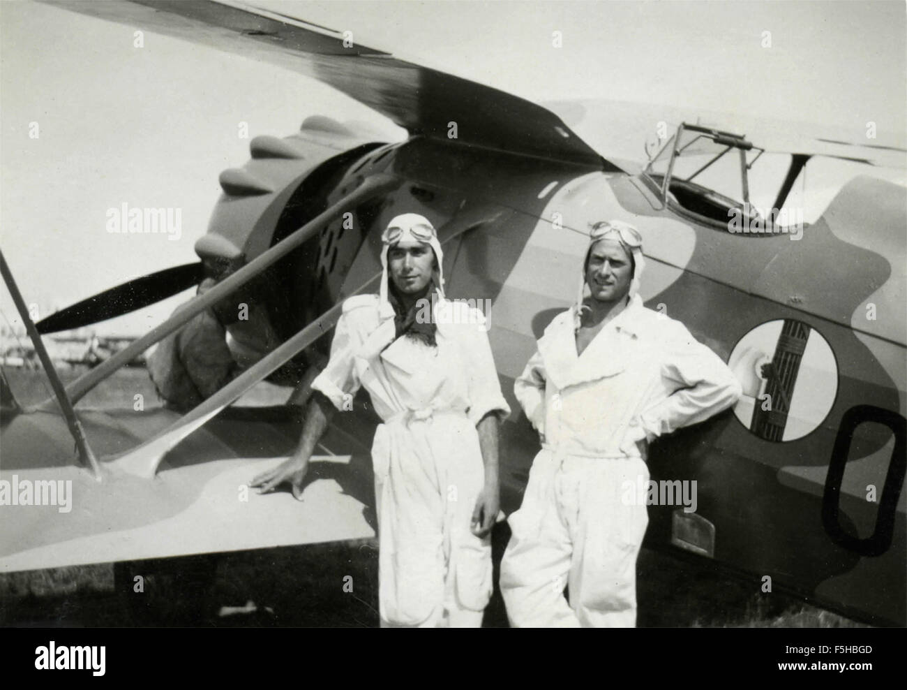 Dos aviadores en traje blanco junto a un avión con un emblema de la viga, Italia Foto de stock