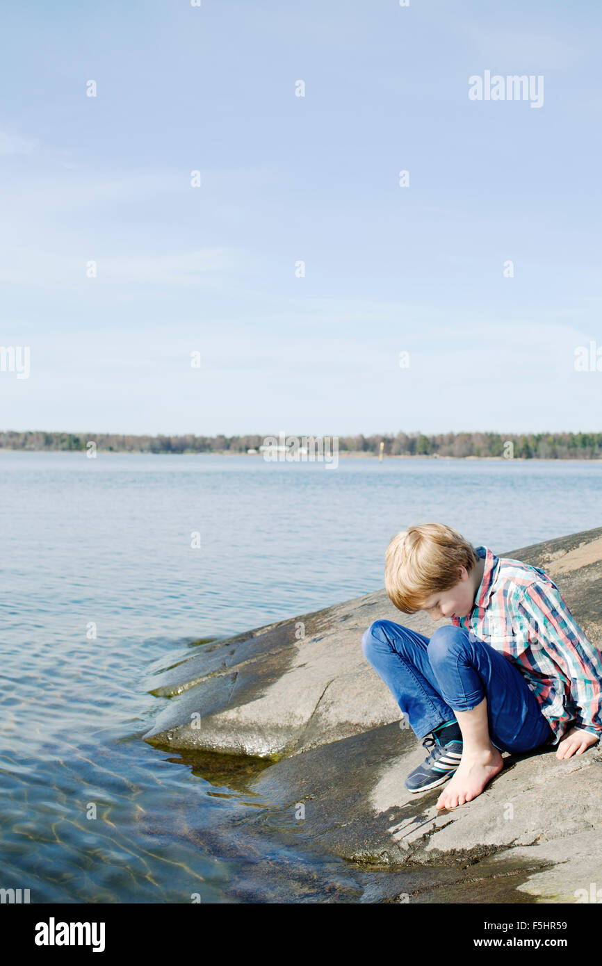 Suecia, Uppland Oregrund, Boy (8-9) Comprobación de la temperatura del agua del mar con su pie. Foto de stock