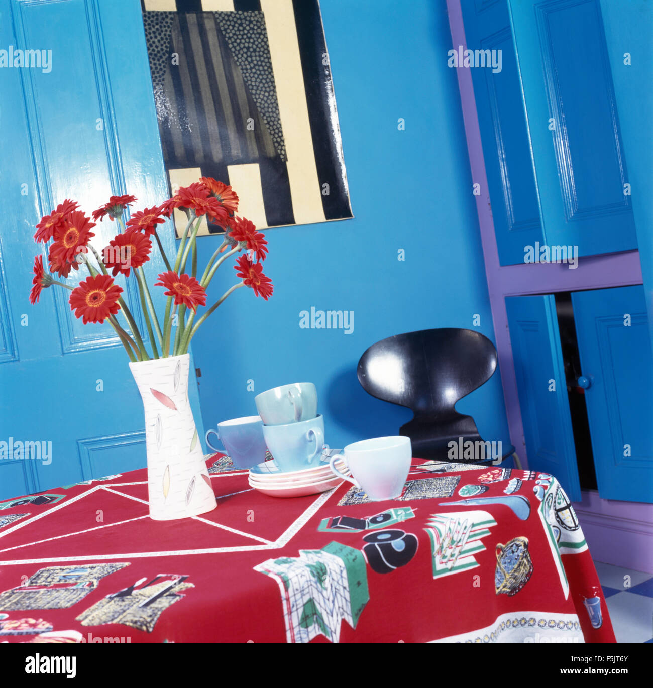 Jarrón de gerberas rojas sobre la mesa con un trapo rojo estampadas en un azul brillante 90 comedor Foto de stock
