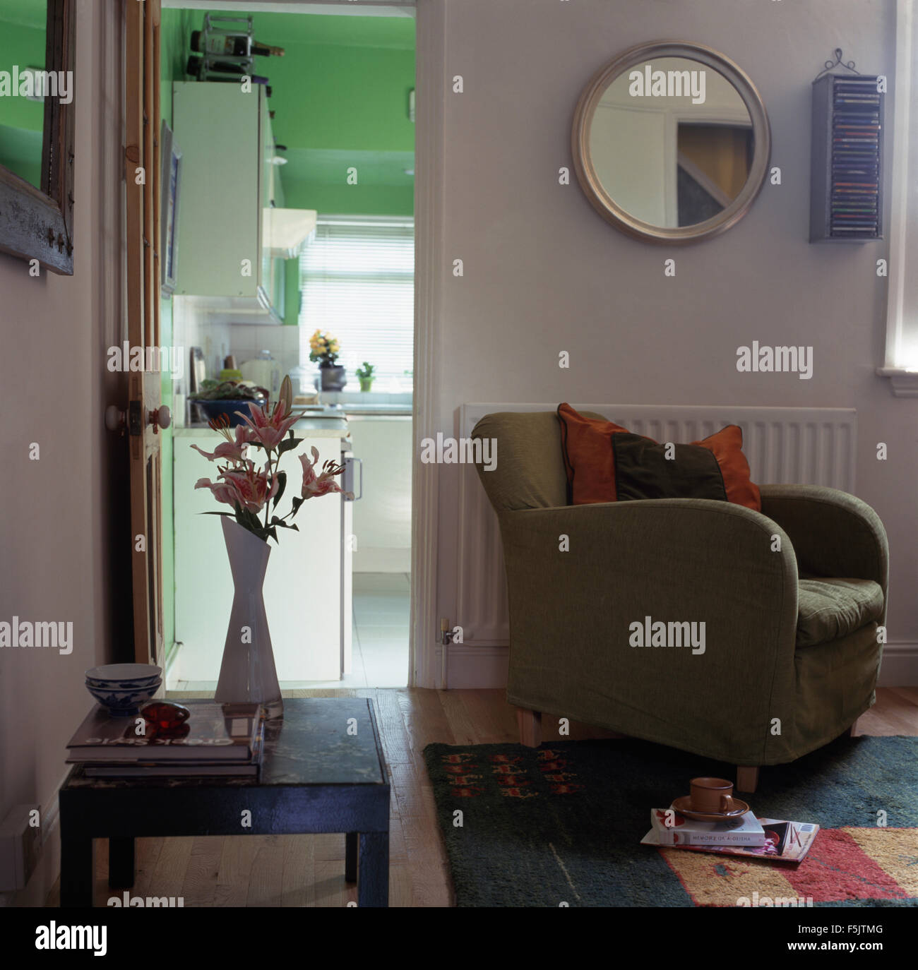 Espejo circular encima de un sillón gris junto a puerta abierta en un salón de estilo economía 90 Foto de stock