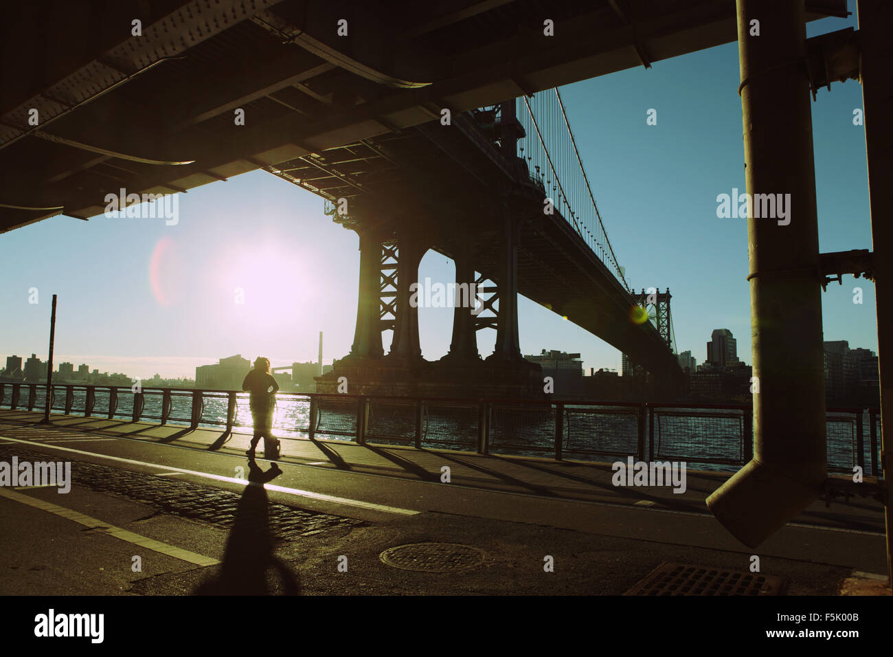 Un corredor avanza hasta el East River Esplanade bajo Manhattan Bridge como el sol sube Foto de stock