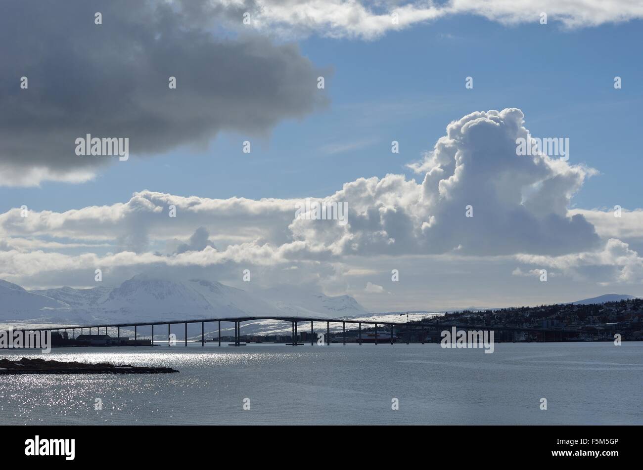 Tromsoe ciudad continental y la conexión de puente sobre el fiordo azul agua, imponentes montañas y telón de fondo del cielo Foto de stock