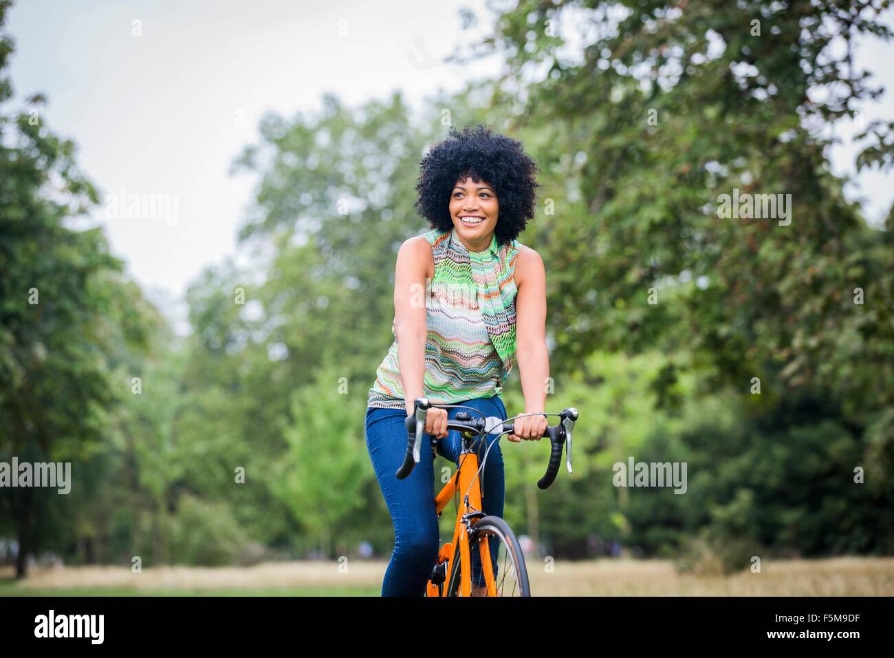 Vista frontal de la mujer madura con afro montando bicicleta mirando lejos sonriendo Foto de stock
