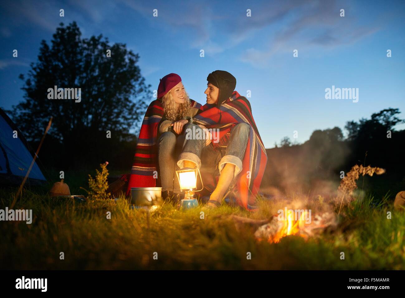 Camping joven pareja sentada por fogata al atardecer Foto de stock