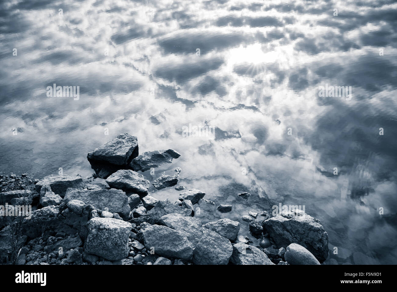 Sigue la costa del lago, las piedras costeras y cielo nublado del reflejo en el agua, Monocromo foto Foto de stock