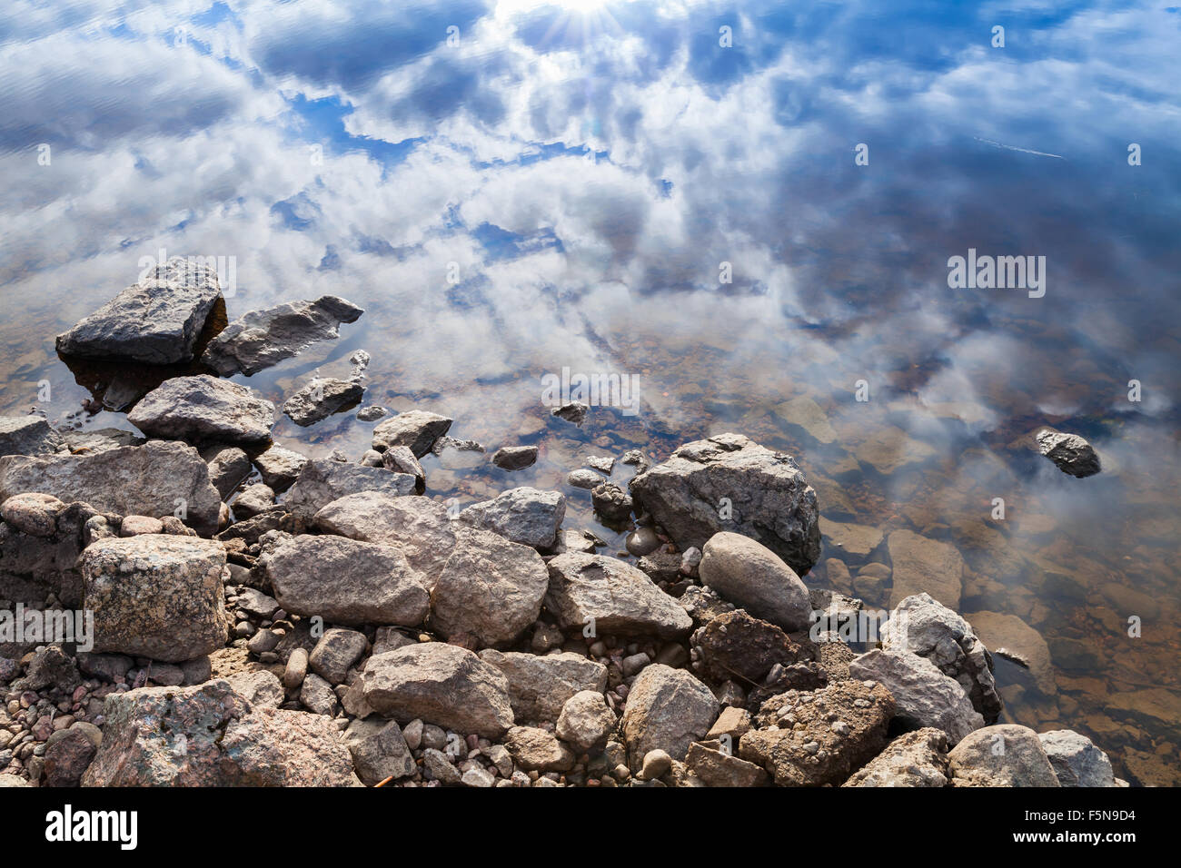 Sigue la costa del lago, las piedras y costa azul cielo nublado del reflejo en el agua Foto de stock