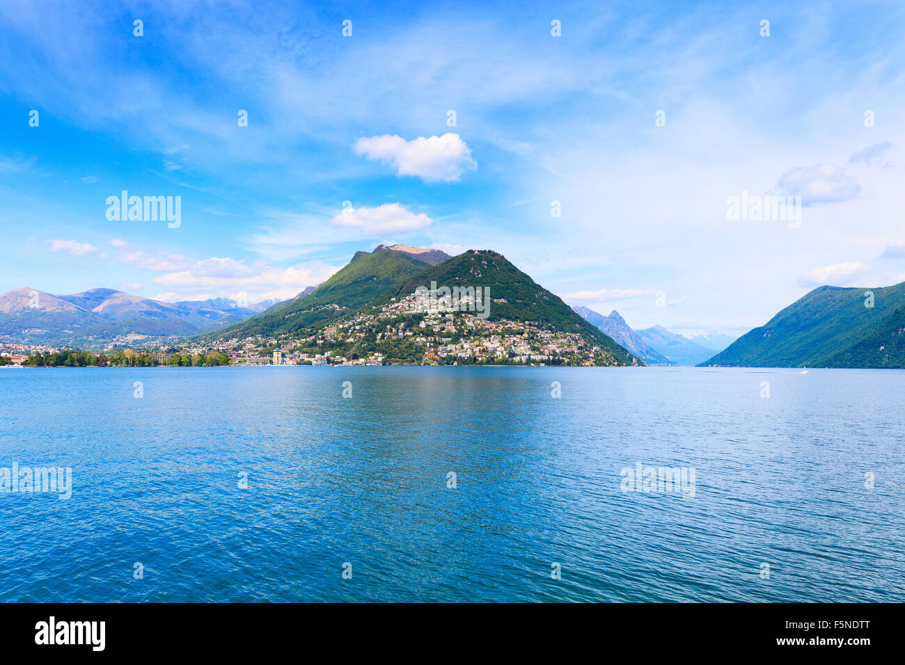 Paisaje del lago de Lugano. Ciudad, el agua del lago, el cielo azul y las montañas. El Tesino, Suiza o en Suiza, Europa. Foto de stock