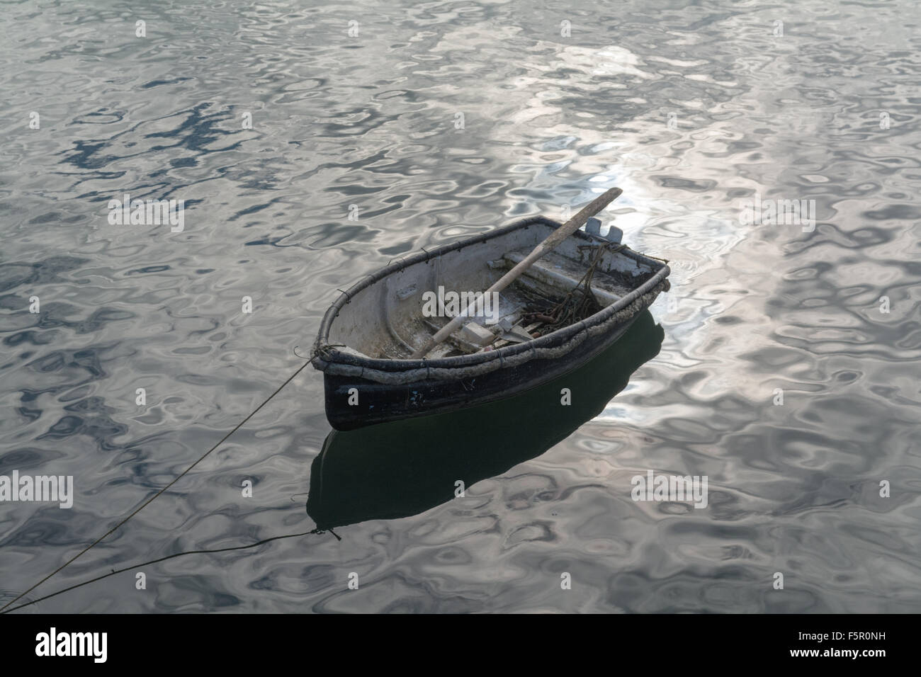 Pequeño y antiguo bote a remo en un puerto con luz brillante desde la superficie reflectante Foto de stock