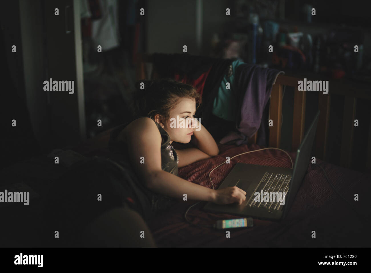 Una adolescente acostada en la cama trabajando en su portátil Foto de stock