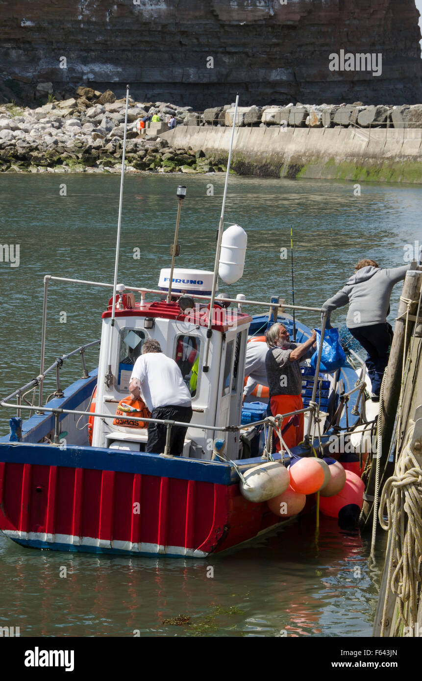 En un día soleado de verano, 4 mar (hombres) los pescadores descargan sus capturas en un barco de pesca atracado en el muelle en Staithes" puerto, North Yorkshire, Reino Unido. Foto de stock