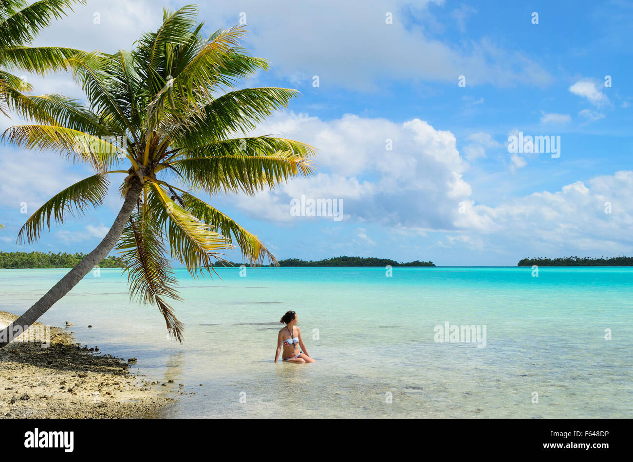 Mujeres turistas bañarse en las aguas poco profundas del mar, debajo de una palmera en una playa en una isla desierta en la laguna de Tahití. Foto de stock