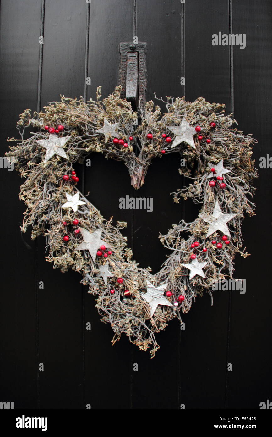 Un rústico en forma de corazón guirnalda de Navidad,o corona, cuelga de una puerta de madera negra en un chalet en el Peak District de Inglaterra Foto de stock