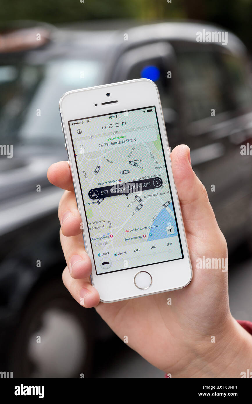 Mano sujetando el iPhone de Apple usando Uber app con taxi negro detrás, Londres, Inglaterra, Reino Unido. Foto de stock