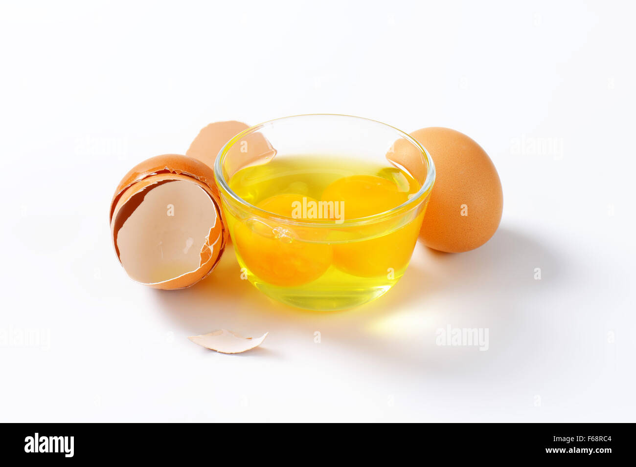 Y yemas de huevo fresco en el tazón de vidrio, un huevo entero y cáscaras de huevo vacías Foto de stock