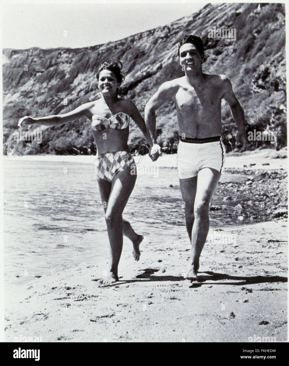 1961, el título de la película: Blue Hawaii, Director: Norman Taurog,  Estudio: Paramount, Foto: pecho desnudo, traje de baño, bañador, Playa,  Joan Blackman, parte del cuerpo, ropa, Elvis Presley, funcionando. (Crédito  de