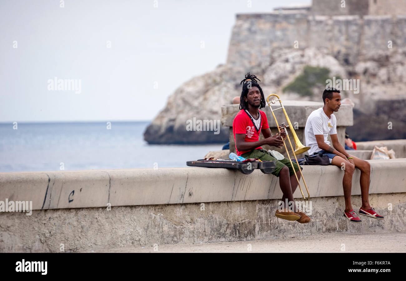 Los adolescentes cubanos a la colocación de los ladrillos del Malecón trombonista, músico afuera con dreadlocks y trombón, escena de una calle, La Habana, C Foto de stock