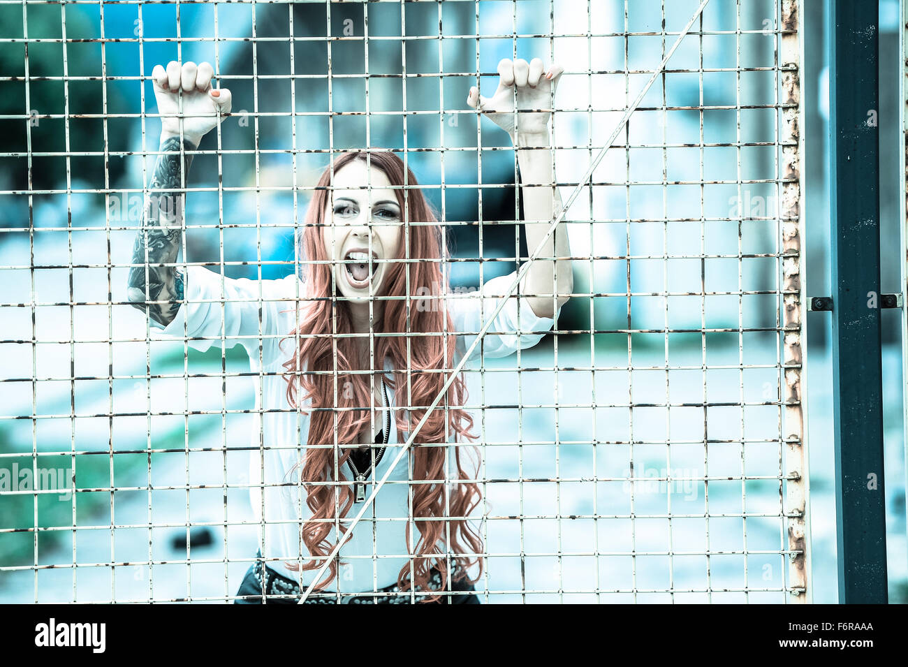 Mujer joven con largo pelo rojo y un tatuaje gritando detrás de las rejas Foto de stock