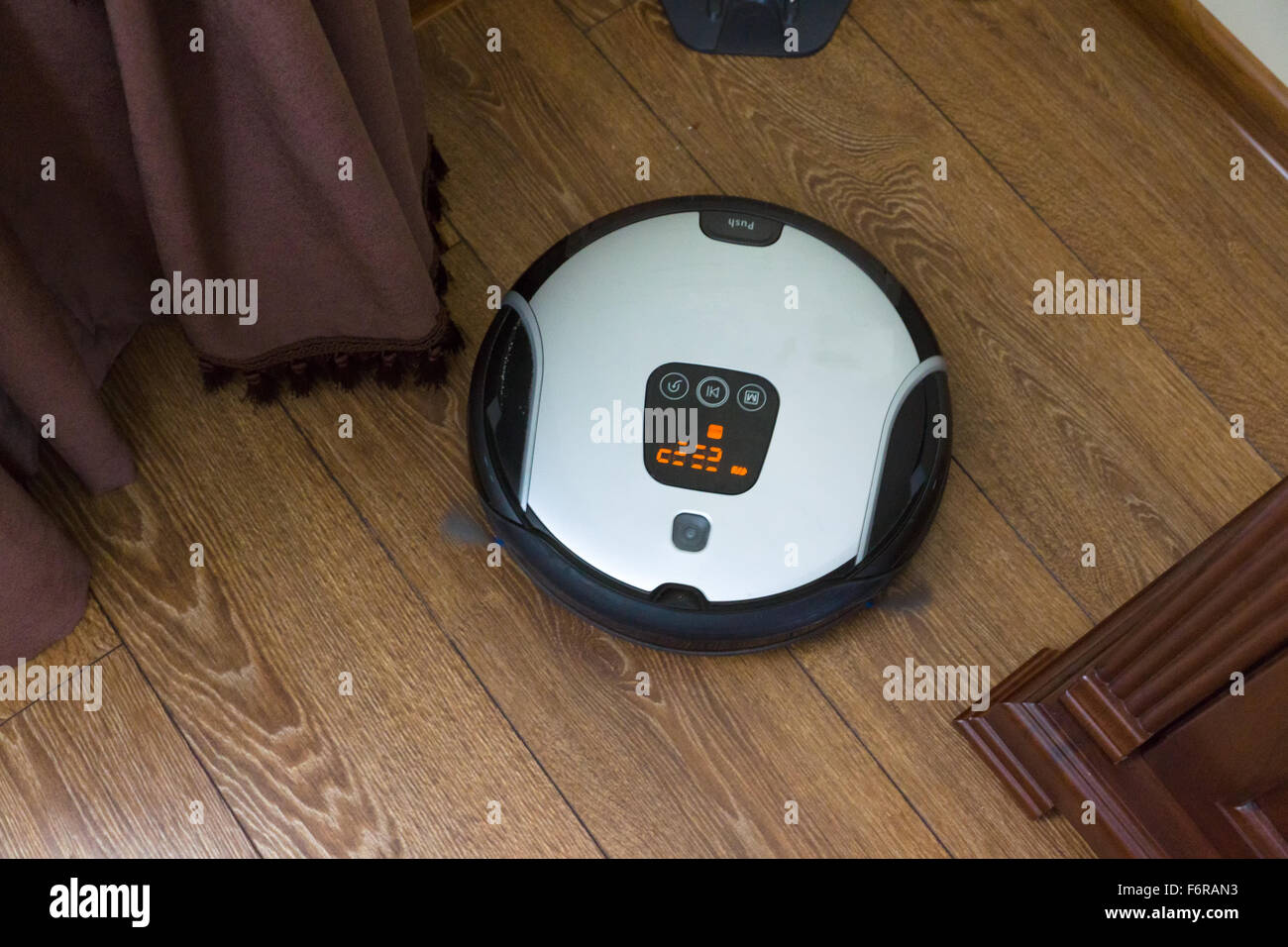 El robot aspirador va sobre un piso sucio y limpia el polvo Foto de stock