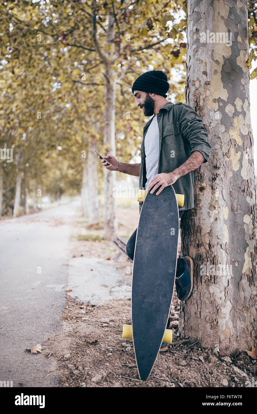 España, Tarragona, hombre joven con longboard RECOSTADA contra el tronco  del árbol mirando a su smartphone Fotografía de stock - Alamy