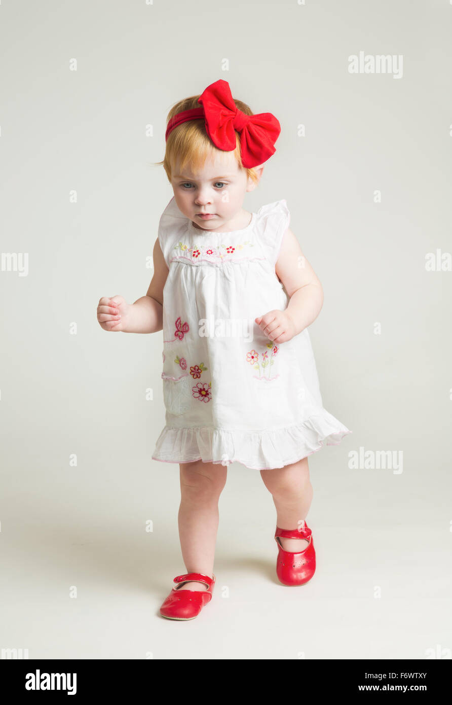 Un pequeño y lindo niña de un año aprendiendo a caminar en zapatos rojos y  arco Fotografía de stock - Alamy