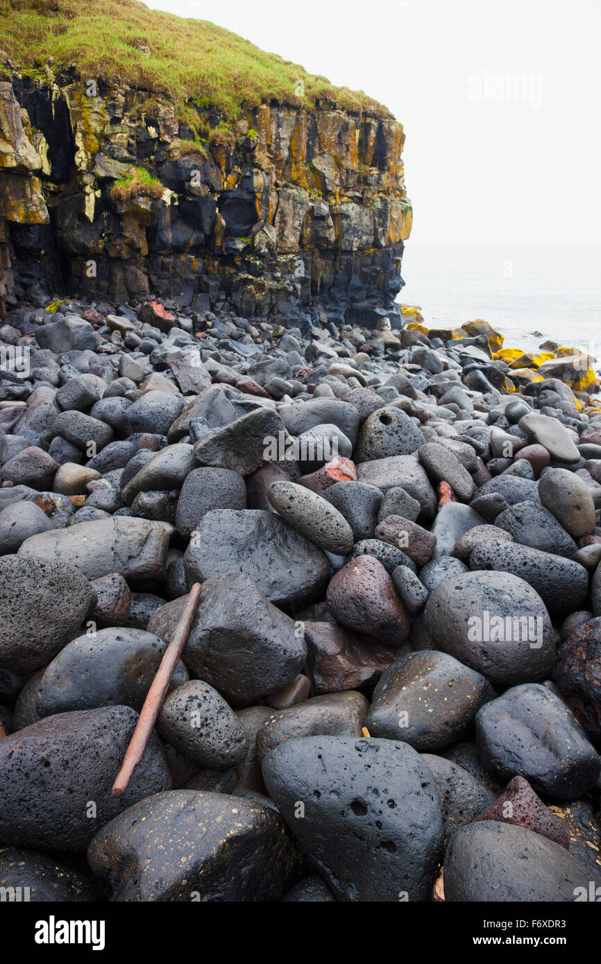 Las rocas volcánicas oscuras a lo largo de la costa del Mar de Bering, con un deterioro en la ladera del acantilado en el fondo, la isla de San Pablo, al suroeste de Alaska, EE.UU., Verano Foto de stock