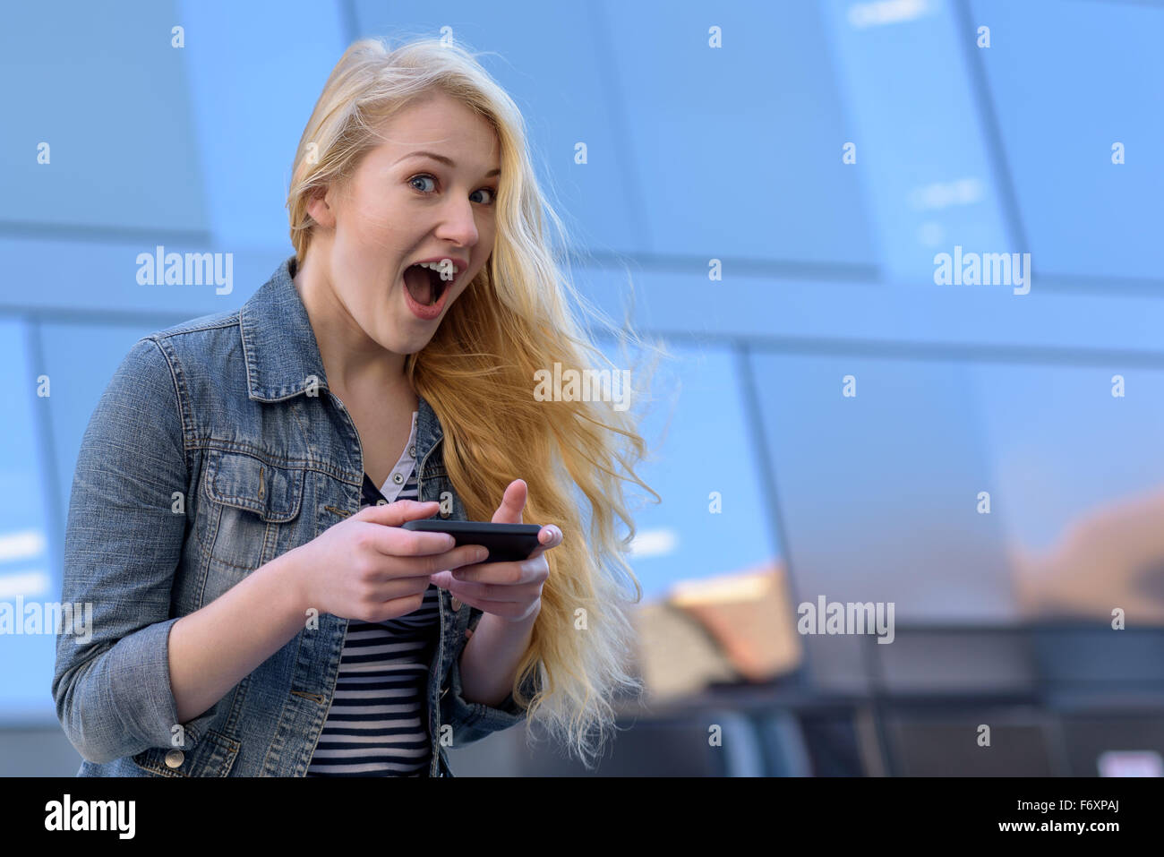 Joven Mujer rubia escribir mensajes de texto con su teléfono móvil con una divertida expresión Foto de stock