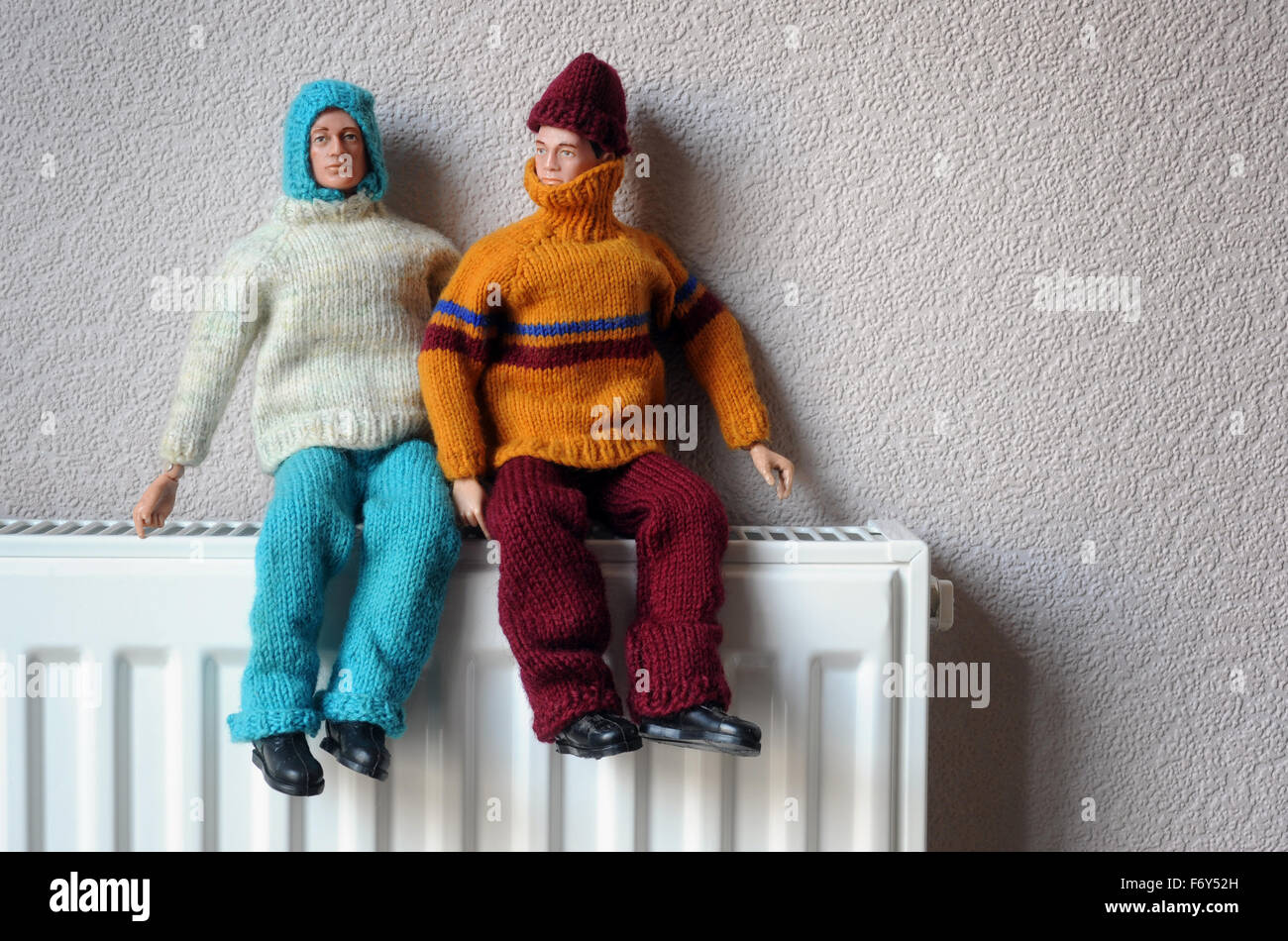 Hombre de acción muñecas en ropa de abrigo sentado en el radiador RE aislamiento doméstico calidez calefacción calderas de gas frío de congelación de la CASA CUESTA UK Foto de stock