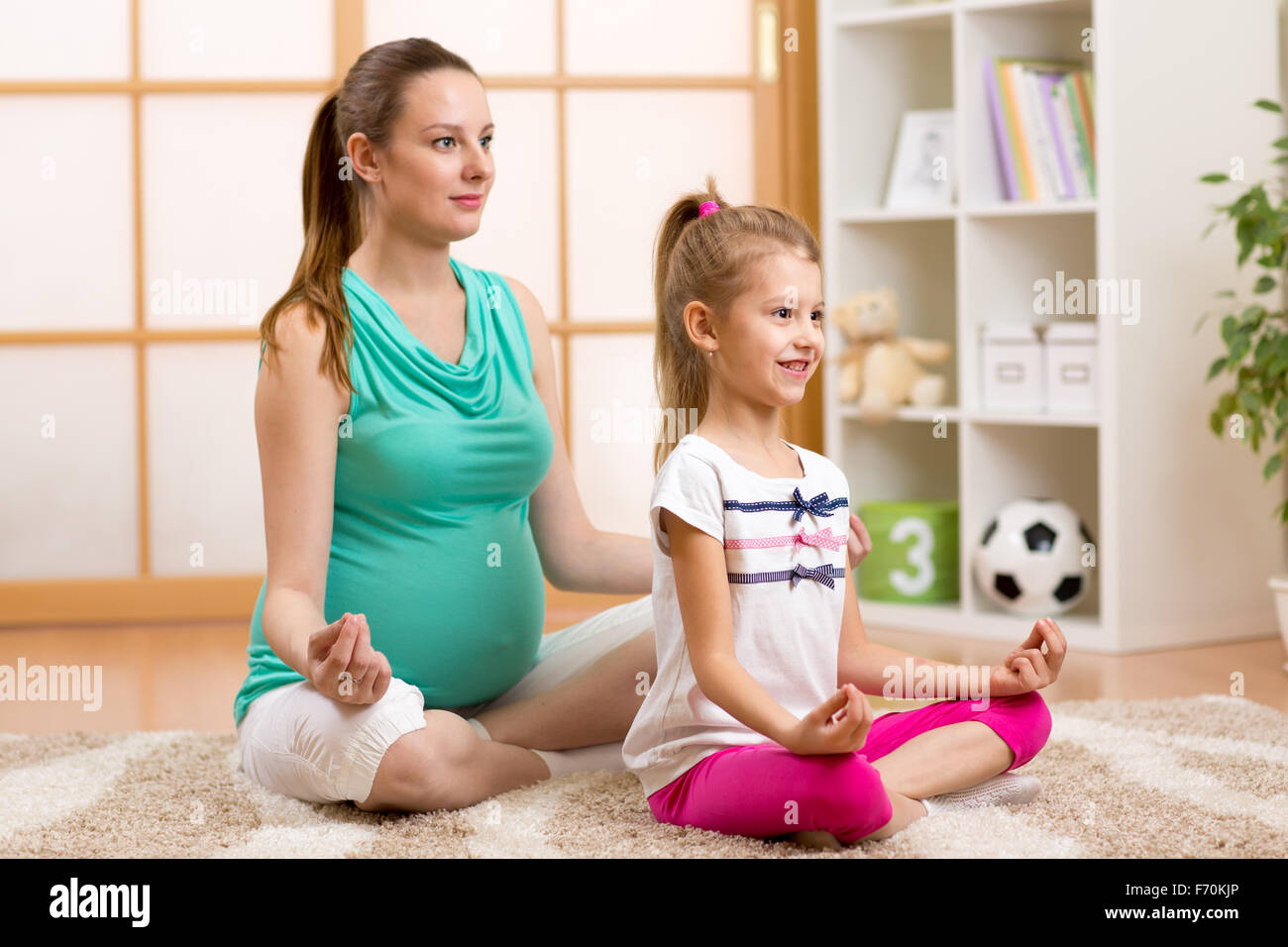 La madre embarazada y del niño hacer yoga, relajarse en la postura del loto en colocar la moqueta en casa Foto de stock