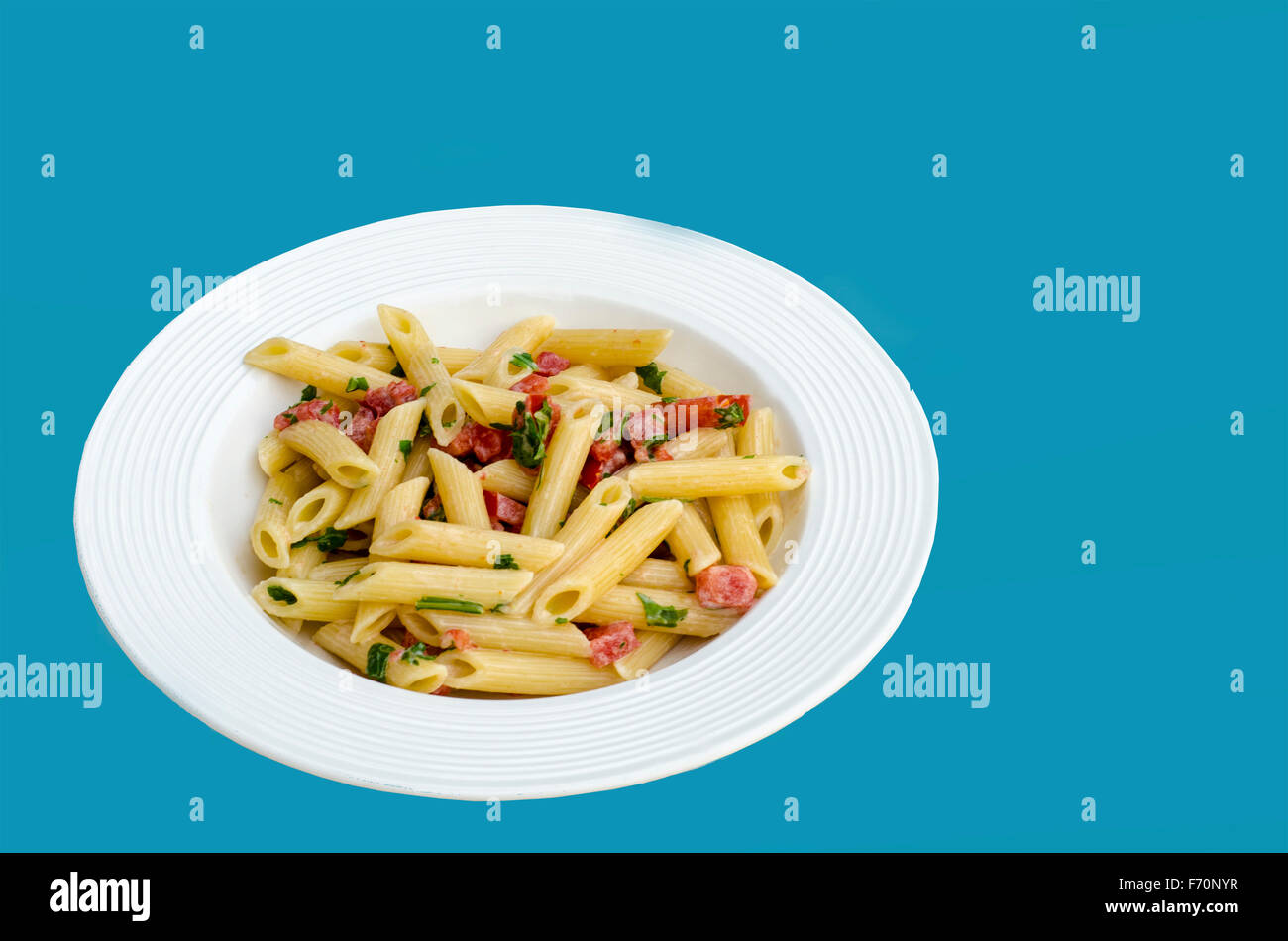 Comida italiana: Pasta llamados mezze pennette con tomates en trozos y arugula. Manjar blanco en fondo azul. Foto de stock