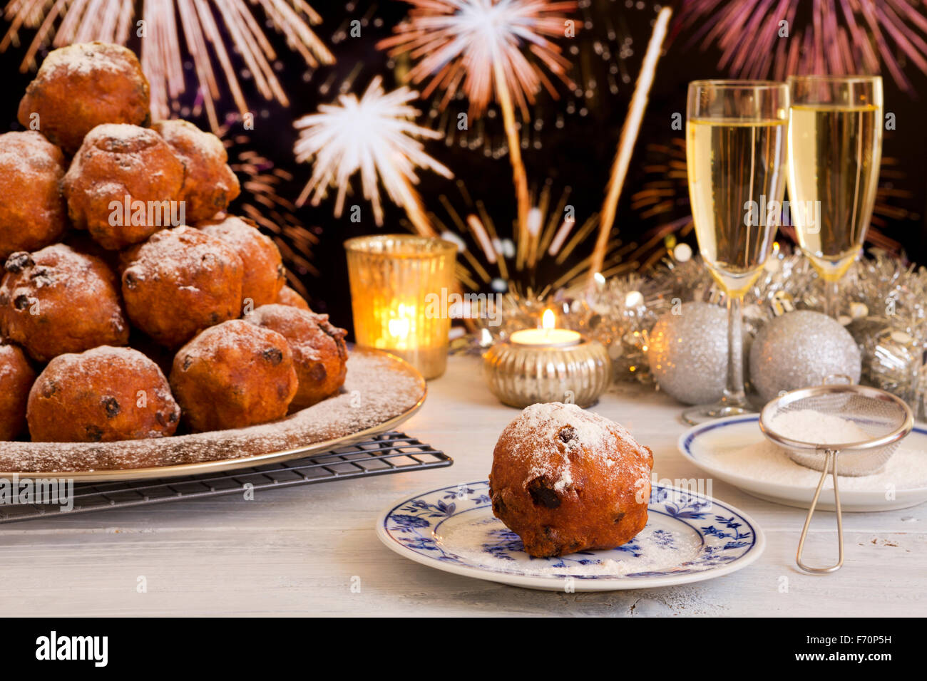 'Oliebollen', repostería tradicional holandés para la Víspera del Año Nuevo. Con champán y fuegos artificiales en el fondo. Foto de stock