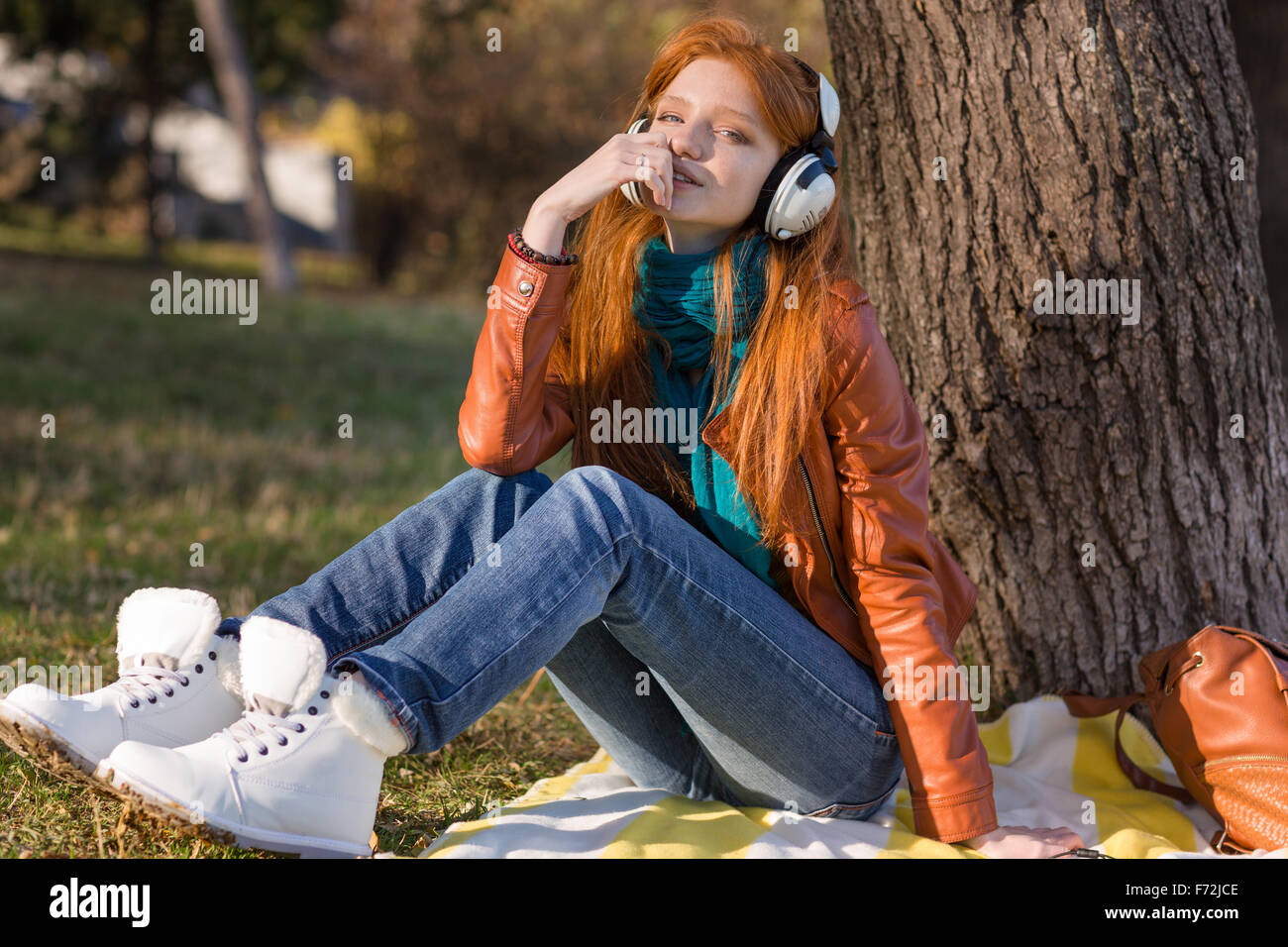 Bastante pensativo joven en chaqueta de cuero, botas blancas y jeans de  escuchar música bajo el árbol Fotografía de stock - Alamy