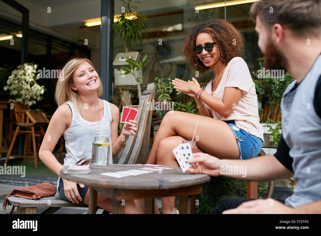 Tres amigos sentado en la cafetería al aire libre y jugar a las cartas y a  divertirse. Los jóvenes feliz en la cafetería en la acera disfrutando jugar  Fotografía de stock - Alamy