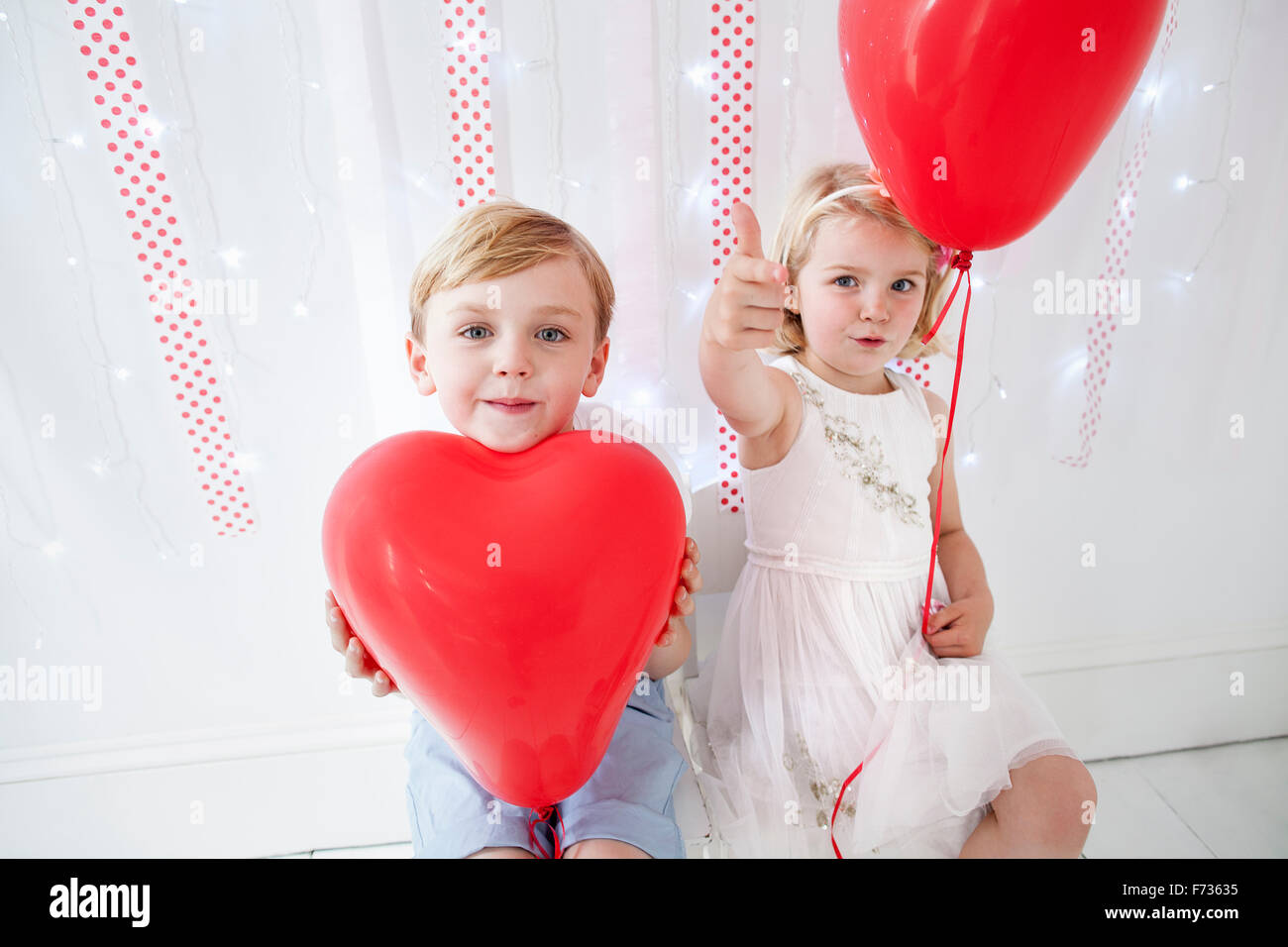 Chico y chica posando para una foto en un estudio del fotógrafo, sosteniendo los globos rojos. Foto de stock