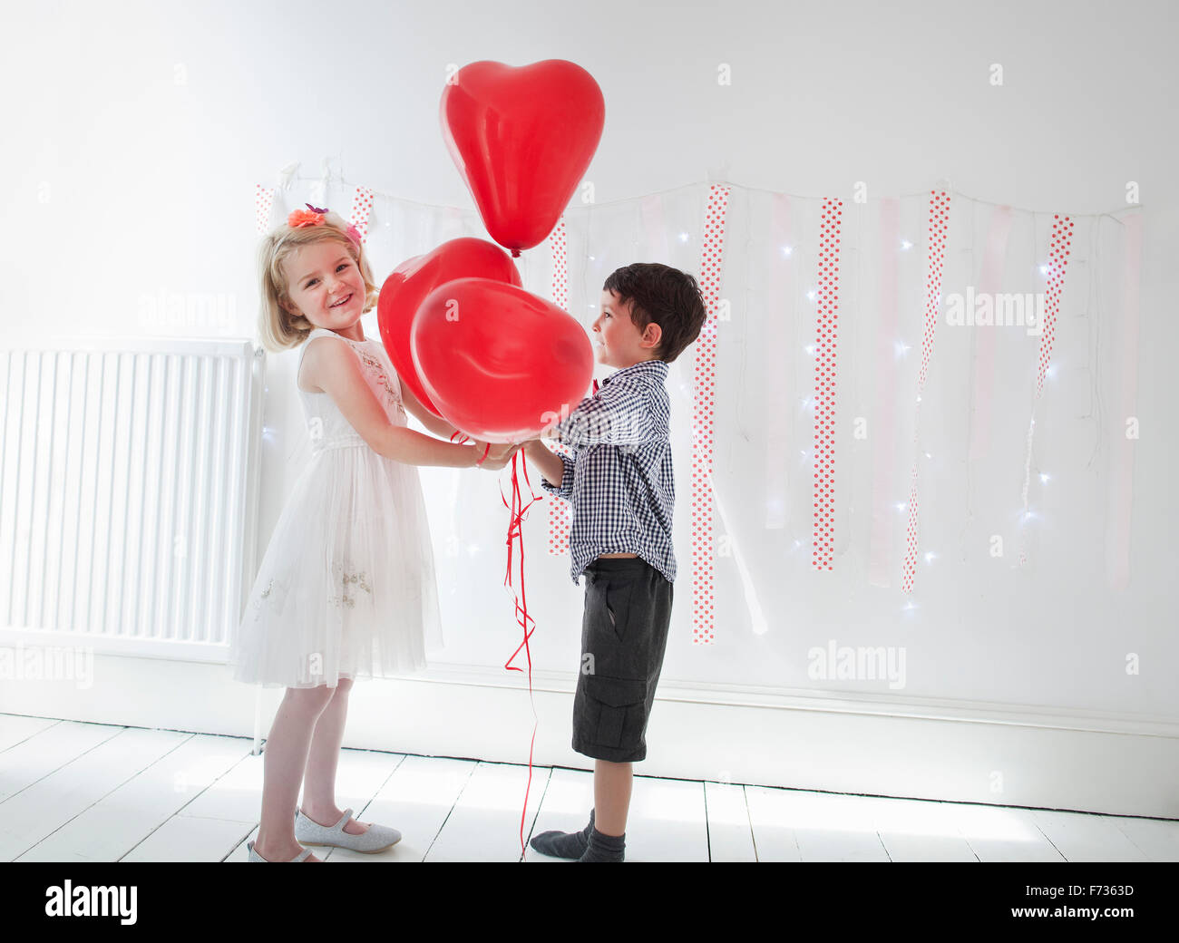 Chico y chica posando para una foto en un estudio del fotógrafo, sosteniendo los globos rojos. Foto de stock